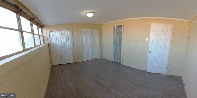 unfurnished bedroom featuring multiple closets, lofted ceiling, dark hardwood / wood-style flooring, and crown molding