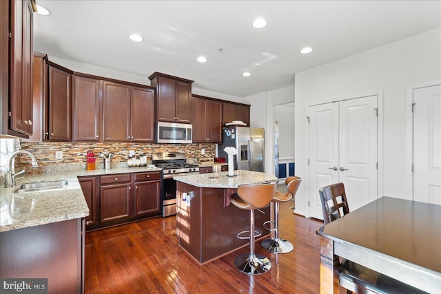 kitchen with a sink, stainless steel appliances, light stone countertops, and dark wood finished floors