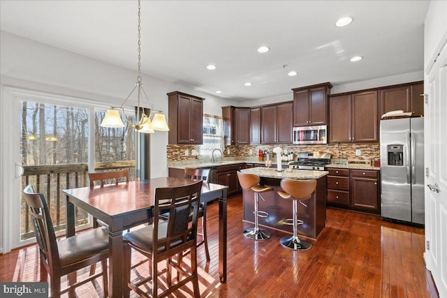 kitchen with dark wood-style floors, a kitchen island, stainless steel appliances, dark brown cabinets, and backsplash