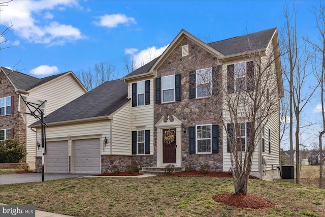 colonial inspired home with aphalt driveway, an attached garage, stone siding, and a front lawn