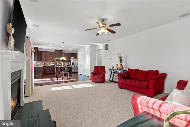 living area featuring visible vents, recessed lighting, ceiling fan, a glass covered fireplace, and dark colored carpet