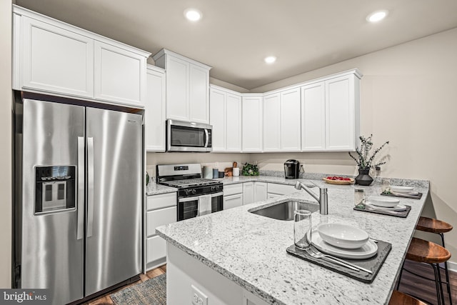 kitchen with a breakfast bar, light stone counters, appliances with stainless steel finishes, kitchen peninsula, and white cabinets