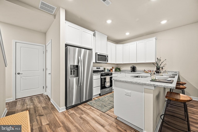 kitchen with sink, light stone counters, appliances with stainless steel finishes, kitchen peninsula, and white cabinets