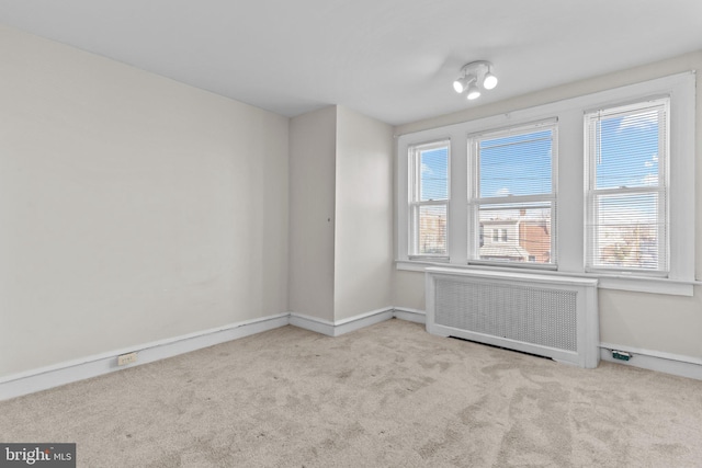 spare room featuring radiator and light carpet