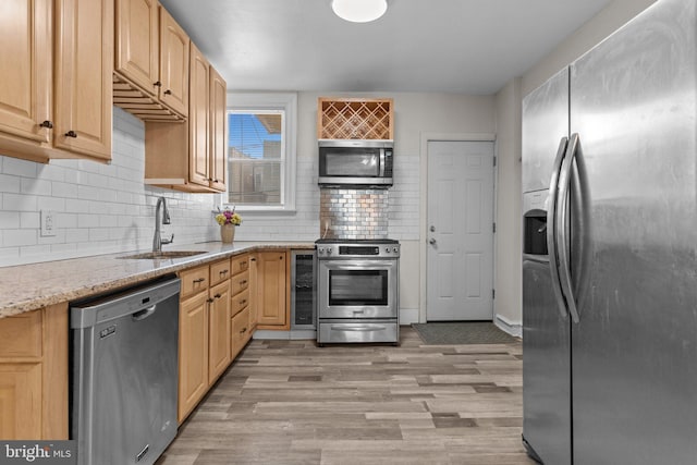 kitchen with sink, appliances with stainless steel finishes, light stone counters, light brown cabinetry, and beverage cooler