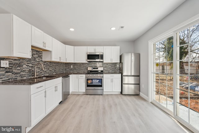 kitchen with appliances with stainless steel finishes, sink, white cabinets, decorative backsplash, and light wood-type flooring