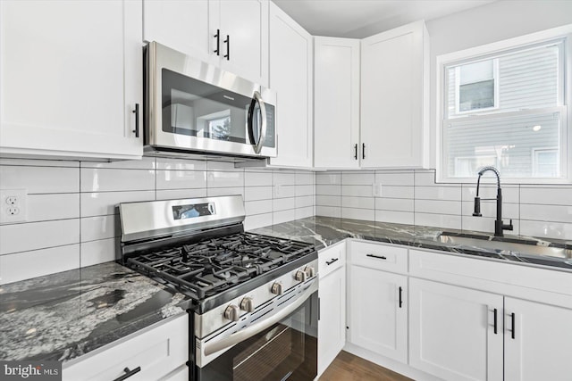 kitchen featuring sink, white cabinetry, dark stone counters, stainless steel appliances, and decorative backsplash