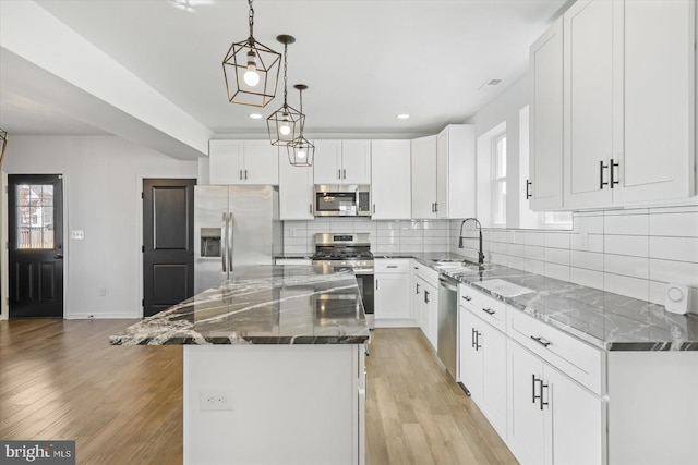 kitchen with appliances with stainless steel finishes, white cabinetry, hanging light fixtures, dark stone countertops, and a center island