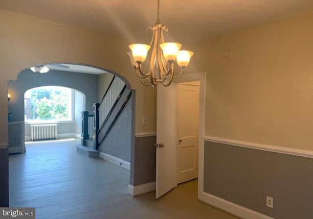 unfurnished dining area featuring an inviting chandelier, radiator heating unit, and wood-type flooring