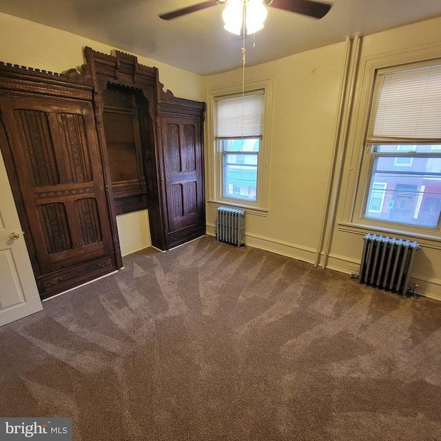 unfurnished bedroom with dark colored carpet, radiator heating unit, and ceiling fan