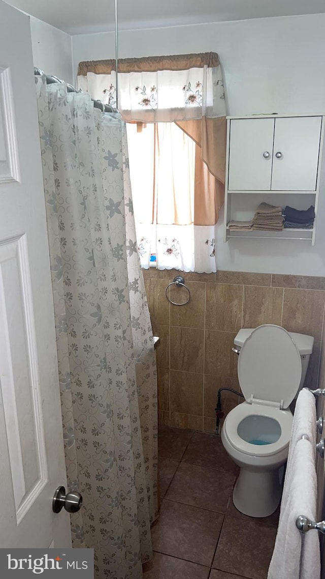 bathroom with tile patterned flooring, tile walls, curtained shower, and toilet