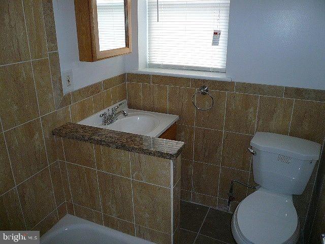 bathroom with a tub, sink, tile walls, and toilet