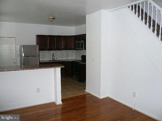 kitchen with stove, hardwood / wood-style flooring, stainless steel fridge, and dark brown cabinetry