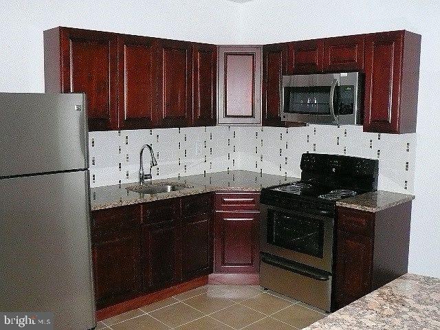 kitchen with sink, appliances with stainless steel finishes, light stone countertops, light tile patterned flooring, and decorative backsplash