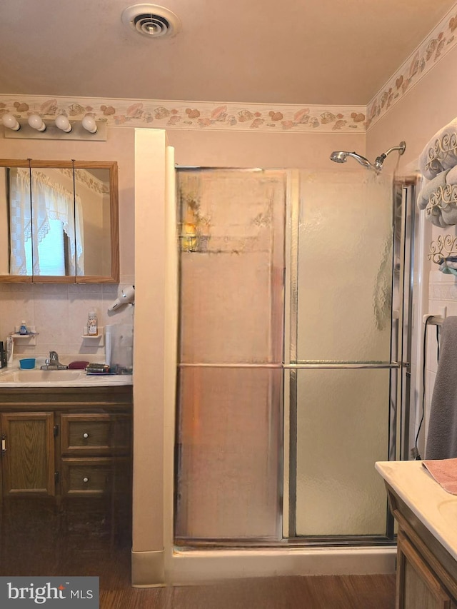 bathroom with vanity, a shower with door, and backsplash