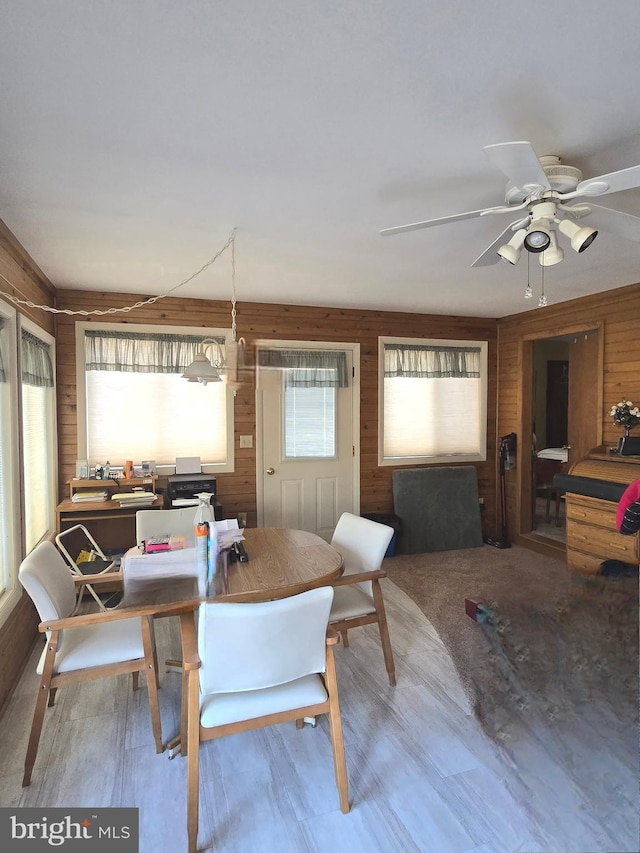 dining space featuring ceiling fan and wooden walls