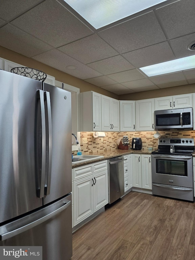 kitchen with sink, hardwood / wood-style flooring, appliances with stainless steel finishes, white cabinets, and decorative backsplash