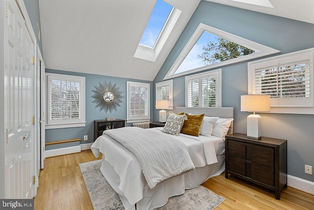 bedroom with a skylight, high vaulted ceiling, and light hardwood / wood-style flooring