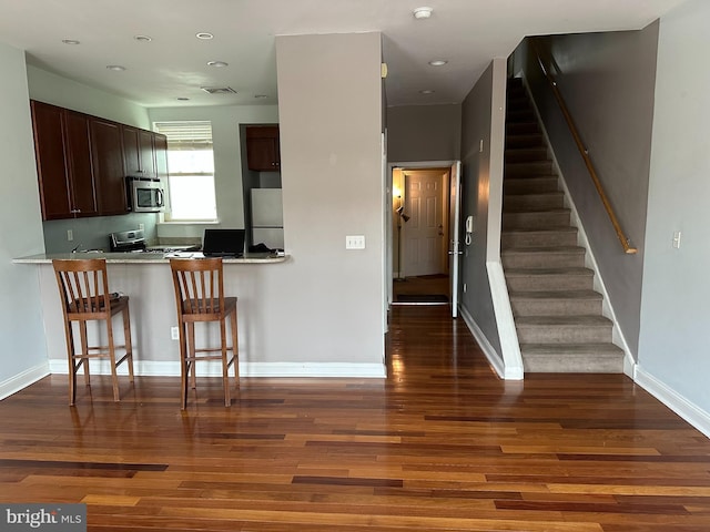 kitchen with fridge, a kitchen bar, dark hardwood / wood-style flooring, and kitchen peninsula