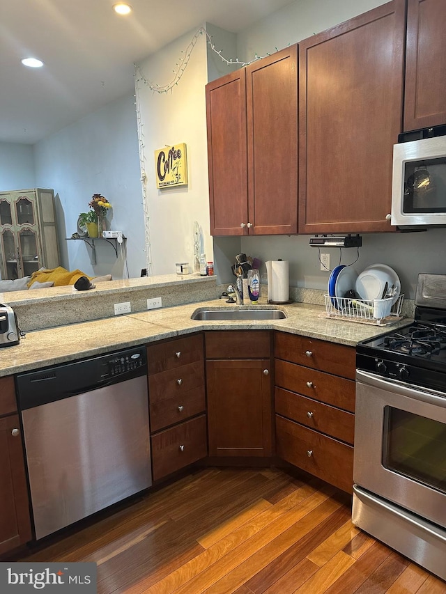 kitchen featuring dark wood-type flooring, sink, kitchen peninsula, stainless steel appliances, and light stone countertops