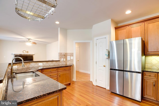 kitchen featuring sink, dark stone counters, light hardwood / wood-style floors, stainless steel refrigerator, and tasteful backsplash