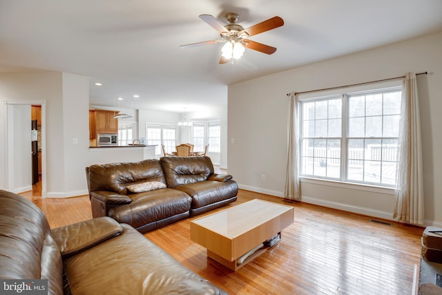 living room featuring light wood-type flooring and ceiling fan with notable chandelier