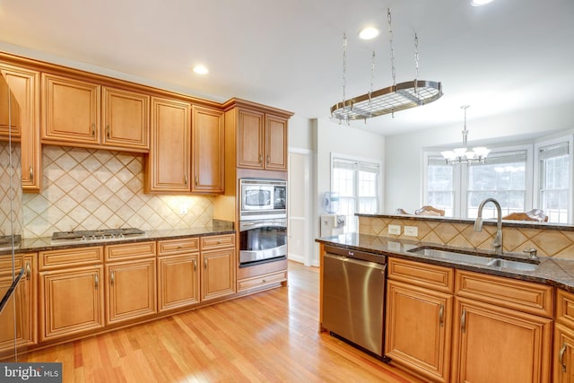 kitchen with light hardwood / wood-style flooring, hanging light fixtures, stainless steel appliances, dark stone counters, and sink