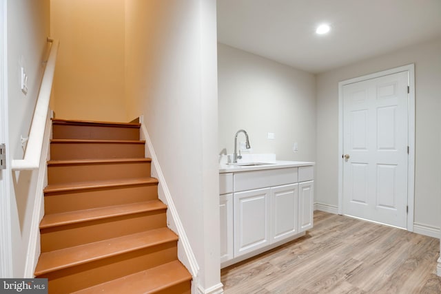 bar featuring light hardwood / wood-style flooring, sink, and white cabinets