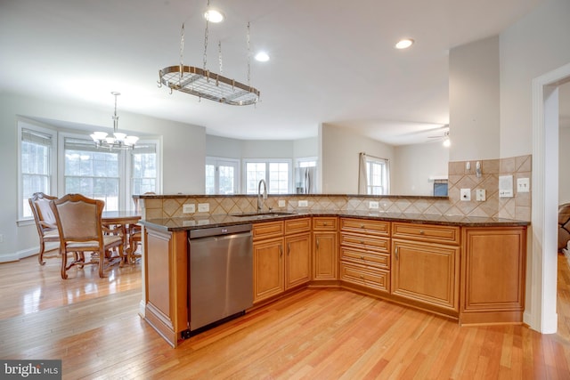 kitchen with sink, backsplash, light wood-type flooring, stainless steel dishwasher, and hanging light fixtures