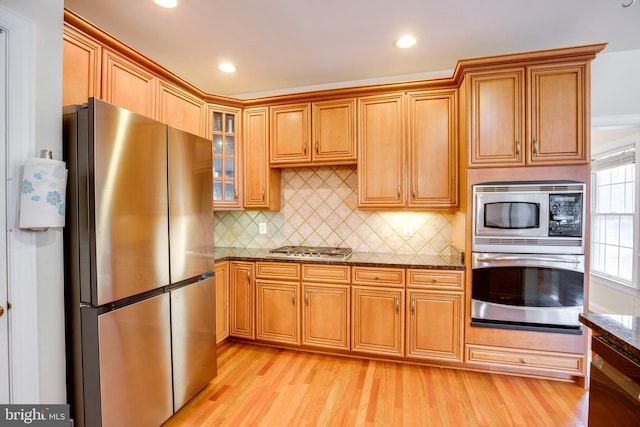 kitchen featuring decorative backsplash, light hardwood / wood-style floors, stainless steel appliances, and dark stone counters