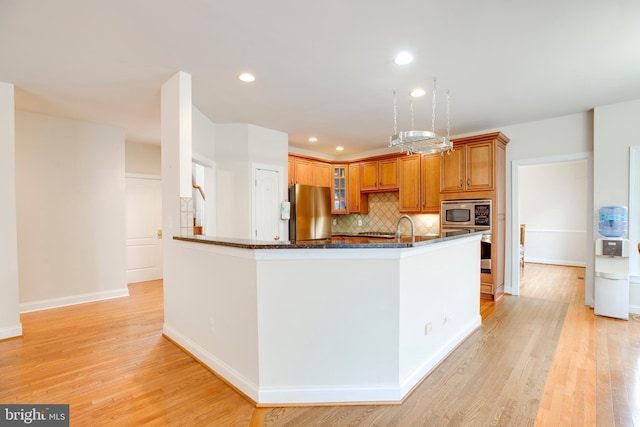 kitchen featuring appliances with stainless steel finishes, dark stone counters, backsplash, light wood-type flooring, and kitchen peninsula