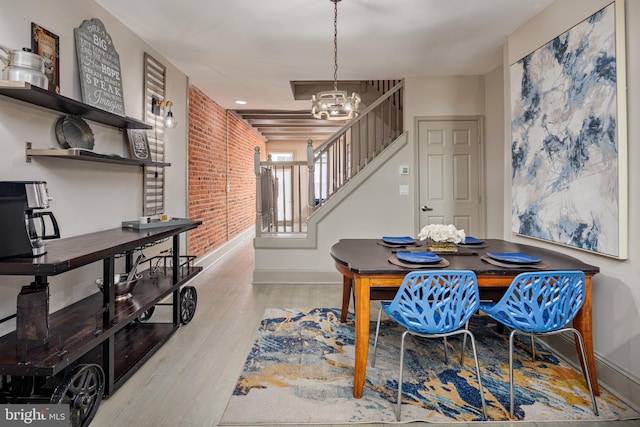 dining space with a notable chandelier, light wood-style flooring, stairway, brick wall, and baseboards