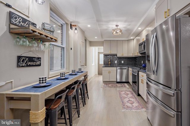 kitchen featuring a sink, appliances with stainless steel finishes, light wood finished floors, dark countertops, and tasteful backsplash