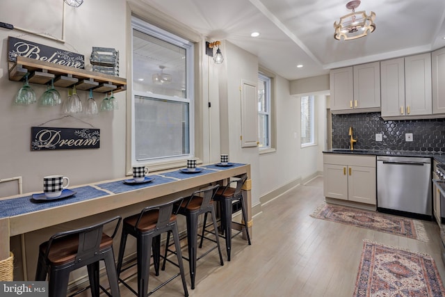 kitchen featuring tasteful backsplash, baseboards, gray cabinets, light wood-style floors, and stainless steel dishwasher