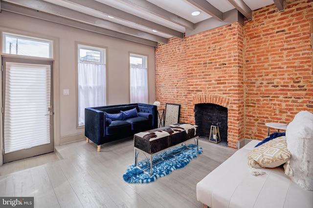 living area with light wood-style floors, a brick fireplace, beamed ceiling, and brick wall