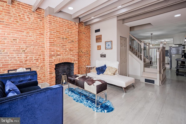 living room with brick wall, stairway, wood finished floors, beamed ceiling, and a brick fireplace