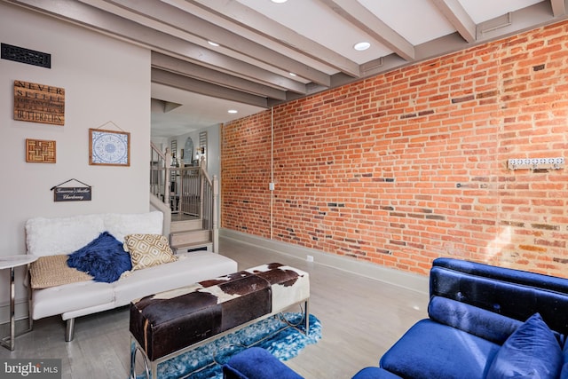 living area with baseboards, brick wall, beamed ceiling, wood finished floors, and stairs