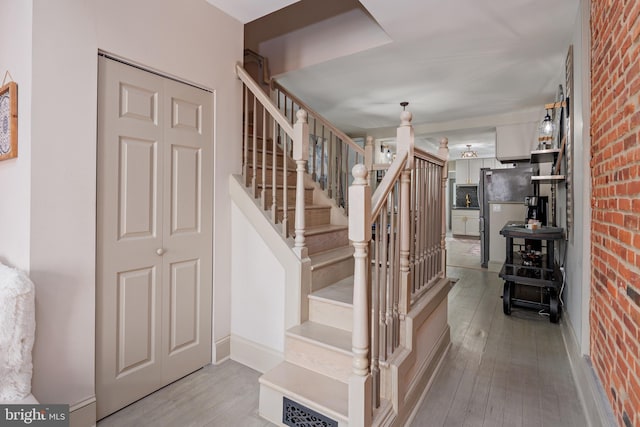 stairway featuring brick wall, baseboards, and wood-type flooring