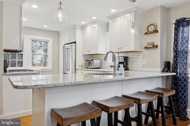 kitchen featuring high end refrigerator, kitchen peninsula, sink, and white cabinets