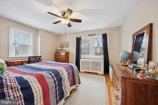 bedroom with multiple windows, radiator, light hardwood / wood-style flooring, and ceiling fan