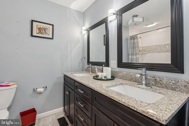 bathroom with double vanity, a sink, toilet, and baseboards