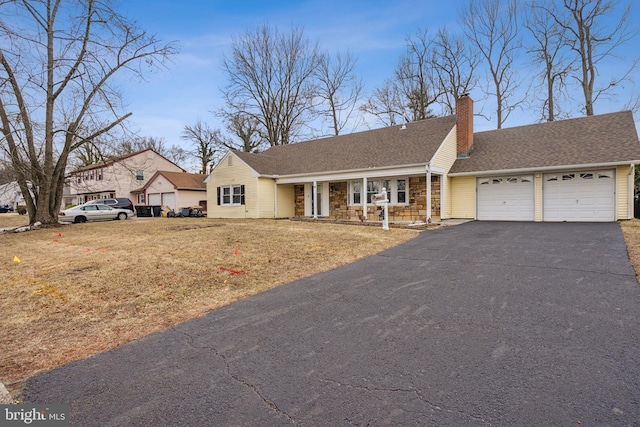 ranch-style house with driveway, a chimney, roof with shingles, an attached garage, and a front lawn