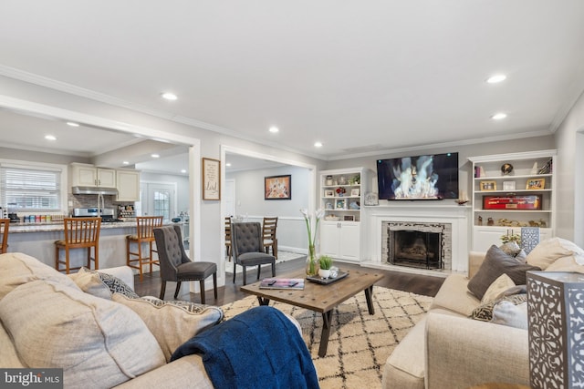 living area featuring a fireplace with raised hearth, ornamental molding, wood finished floors, and recessed lighting