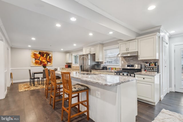 kitchen featuring under cabinet range hood, stainless steel appliances, ornamental molding, backsplash, and dark wood-style floors