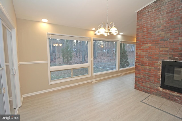 unfurnished living room with a brick fireplace, hardwood / wood-style flooring, and a notable chandelier