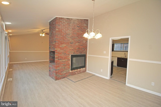 unfurnished living room with lofted ceiling, sink, hardwood / wood-style flooring, ceiling fan, and a brick fireplace