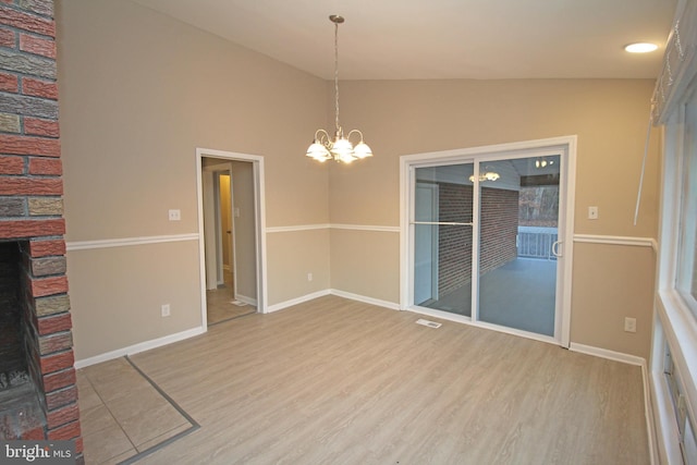 unfurnished dining area featuring a chandelier, a fireplace, light hardwood / wood-style floors, and vaulted ceiling