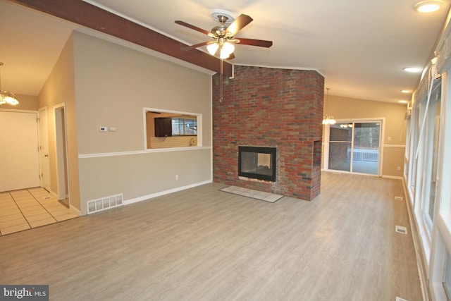 unfurnished living room featuring lofted ceiling, ceiling fan with notable chandelier, a fireplace, and light hardwood / wood-style floors