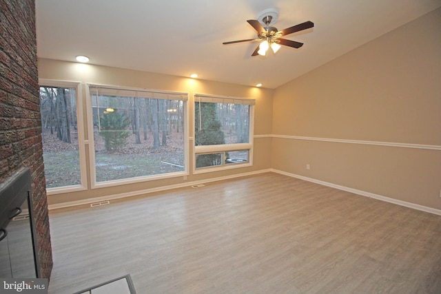 unfurnished living room with wood-type flooring, lofted ceiling, a fireplace, and ceiling fan