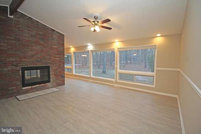 unfurnished living room with hardwood / wood-style flooring, ceiling fan, a fireplace, and lofted ceiling with beams